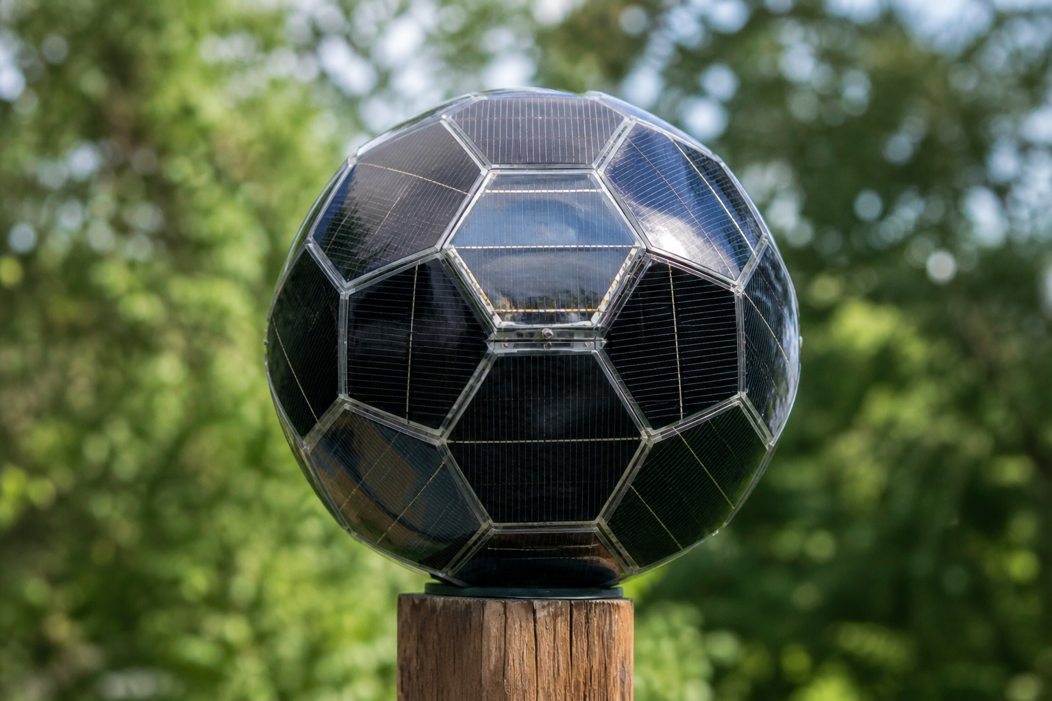 Small DIY solar sphere prototype mounted outdoors on a wooden post, showing multi-faceted photovoltaic cell arrangement in natural daylight