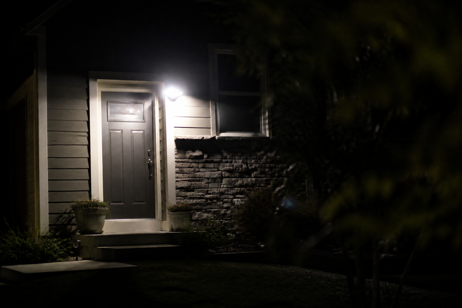 A dark residential exterior at night with a battery-powered motion floodlight illuminating a door, representing grid-down home security