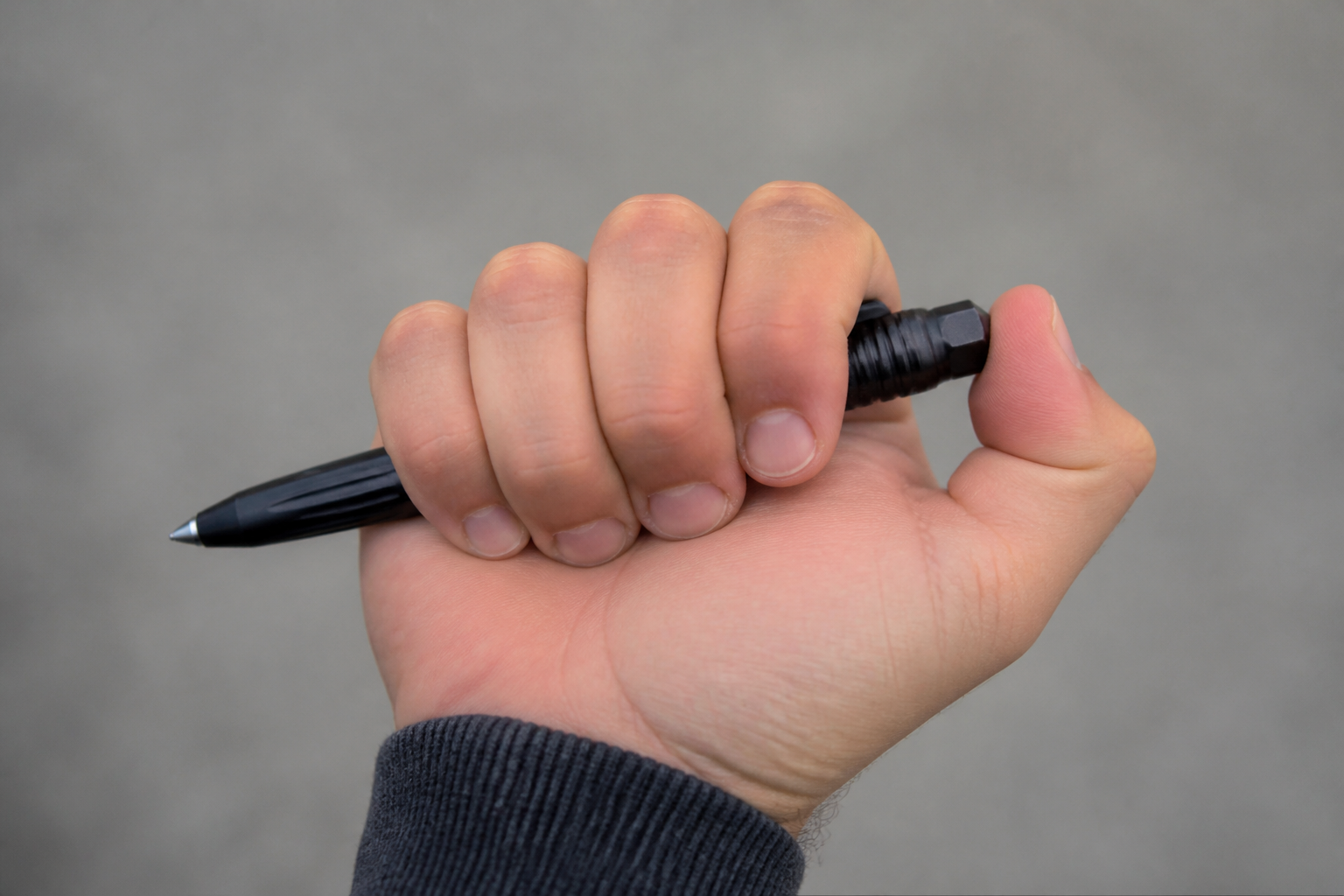 Close-up of a hand gripping a tactical pen in a palm-stick hold, against a neutral background, demonstrating a beginner self-defense grip